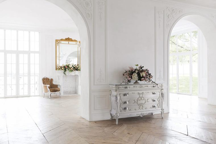Comò laccato bianco con decori, in una stanza luminosa con specchiera dorata